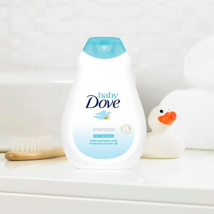 Baby Dove Rich Moisture Shampoo white bottle with teal cap on white surface, rubber duck and brush alongside, white background.