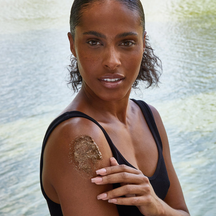 Woman applying body scrub to her shoulder.