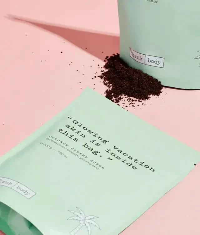 Frank Body Coconut Coffee Scrub 200g mint green bag on pink background with scattered coffee grounds and matching container.