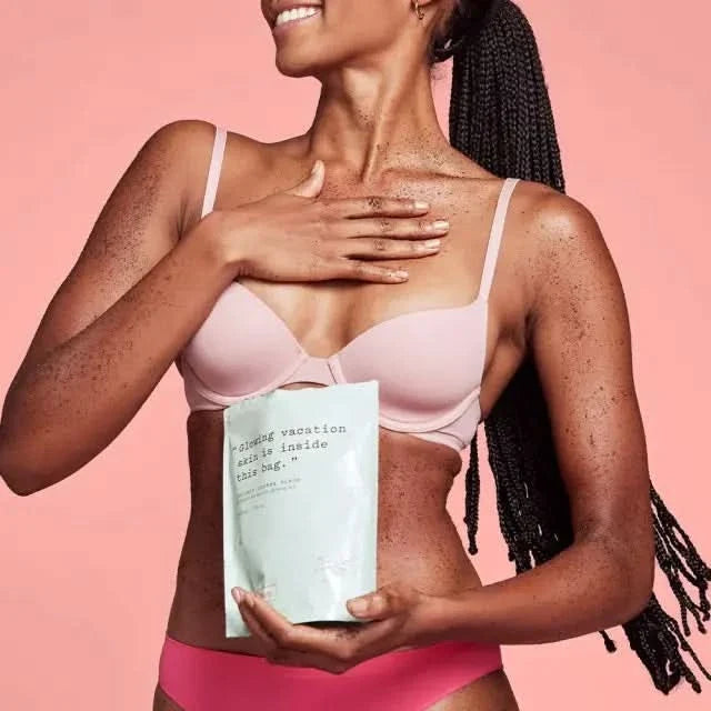 Frank Body Coconut Coffee Scrub 200g held by woman in pink bikini on coral background, package reads "glowing vacation skin is inside this bag"