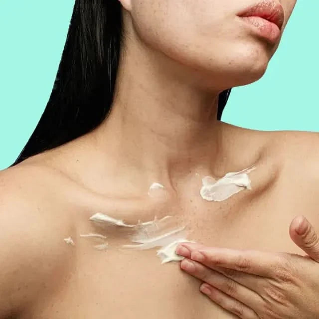 Woman applying Frank Body Smoothing AHA Body Lotion to chest and neck on a teal background.