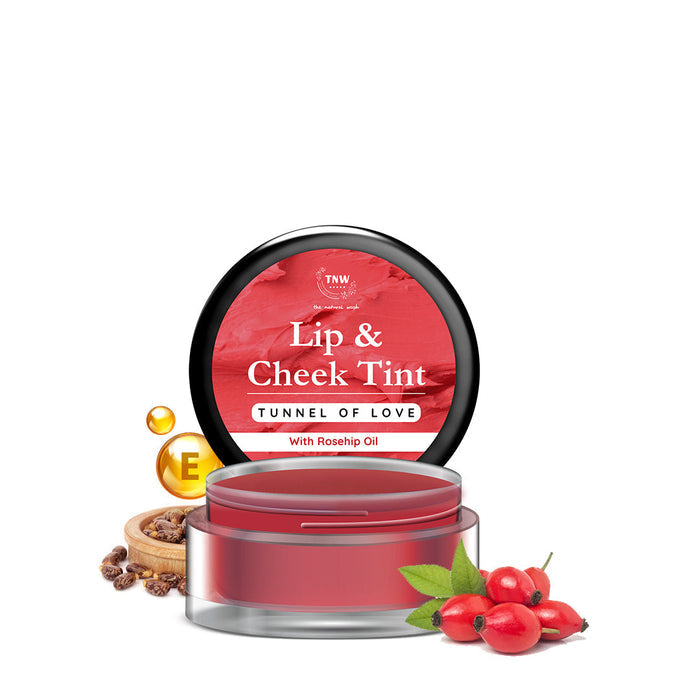 A small open jar of Lip & Cheek Tint with a red label showing 'Tunnel of Love' shade, accompanied by rosehip seeds and a small branch with leaves, indicating natural ingredients.