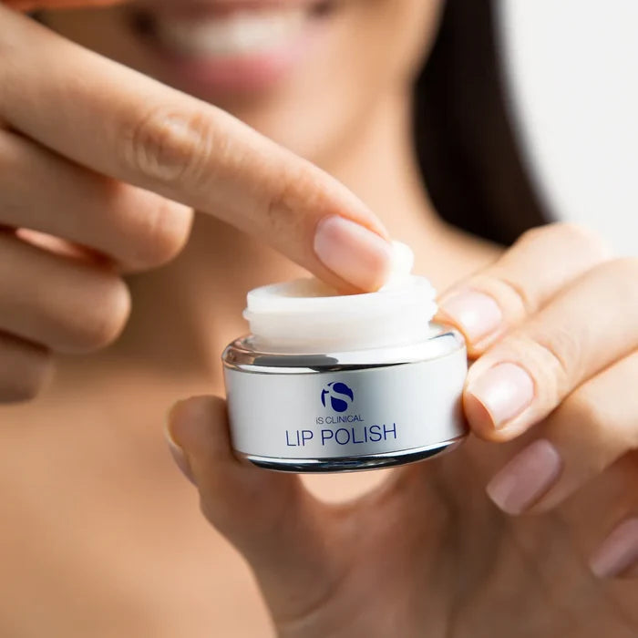 Hand holding open iS Clinical Lip Polish jar with finger dipping into white balm
