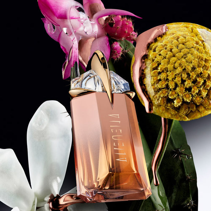 Mugler Alien Goddess Supra Florale EDP 30ml rose-gold bottle with crystal cap, surrounded by pink orchid, white magnolia, yellow flower on black background.