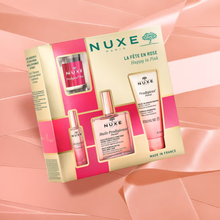 Nuxe Happy In Pink 4 Piece Gift Set box on a peach background, showing Huile Prodigieuse Florale dry oil, candle, perfume and shower gel.