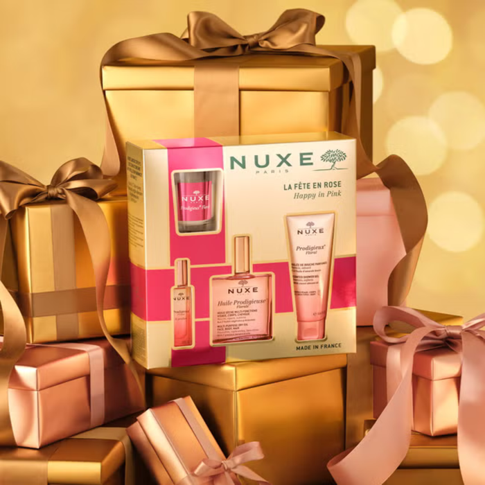 Nuxe Happy In Pink 4 Piece Gift Set box reading "La Fête en Rose" on gold background surrounded by wrapped gifts.