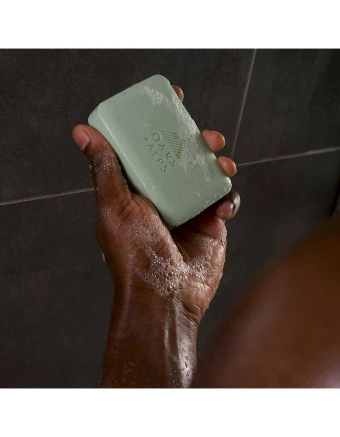 Hand holding Epsom Salt Bar Soap with soap lather in a shower setting