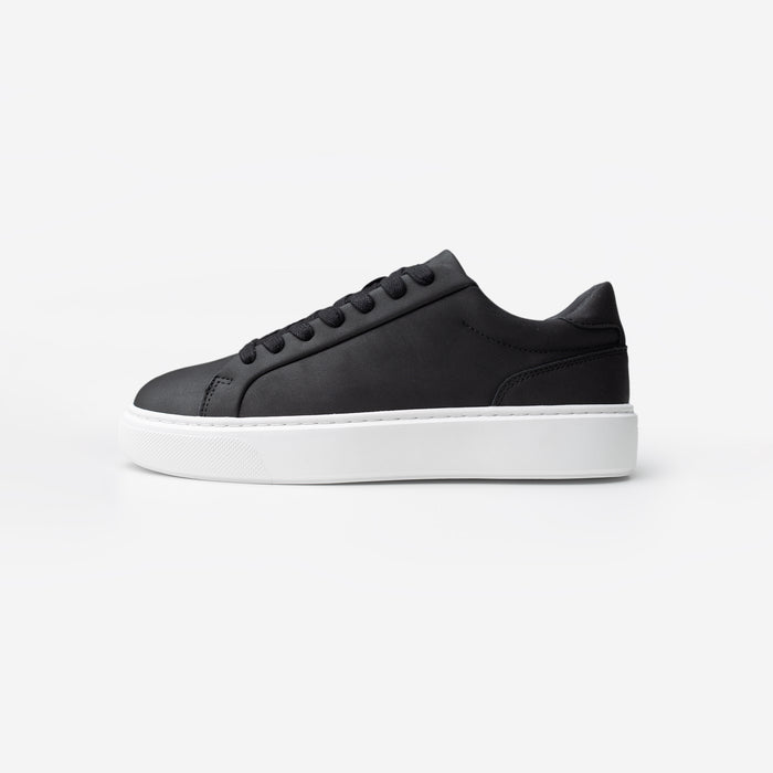 Side view of the Premium Classic Trainer in black, featuring a clean white PU upper, grey faux suede heel, white lace-up fastening and cushioned cup sole.