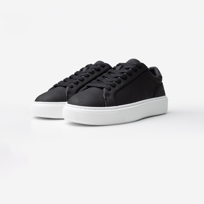 Three-quarter view of the Premium Classic Trainers in black, featuring clean white PU uppers, white lace-up fastening, grey faux suede heel panels and cushioned cup soles.
