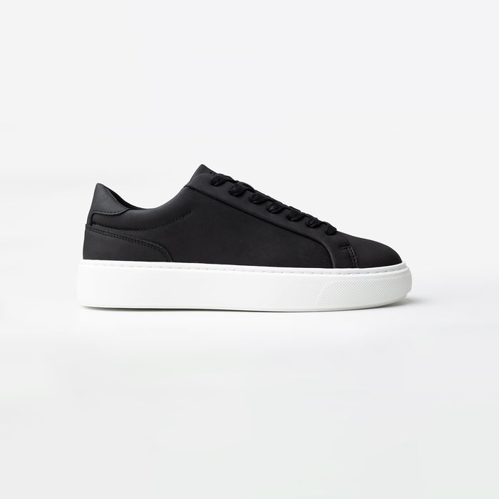Side view of the Premium Classic Trainer in black, featuring a clean white PU upper, grey faux suede heel, white lace-up fastening and cushioned cup sole.