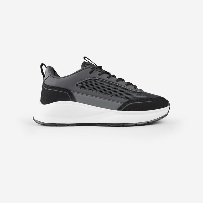 Side shot of black premium trainers with grey panels and white sole, shot on white background
