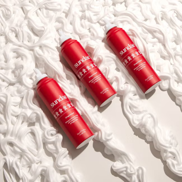 Three red Sundae Gingerbread Shower Foam 265ml cans with white caps on a white foam textured background.