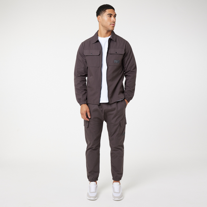 Model wearing brown men's utility cargo pants with matching brown men's zip up overshirt