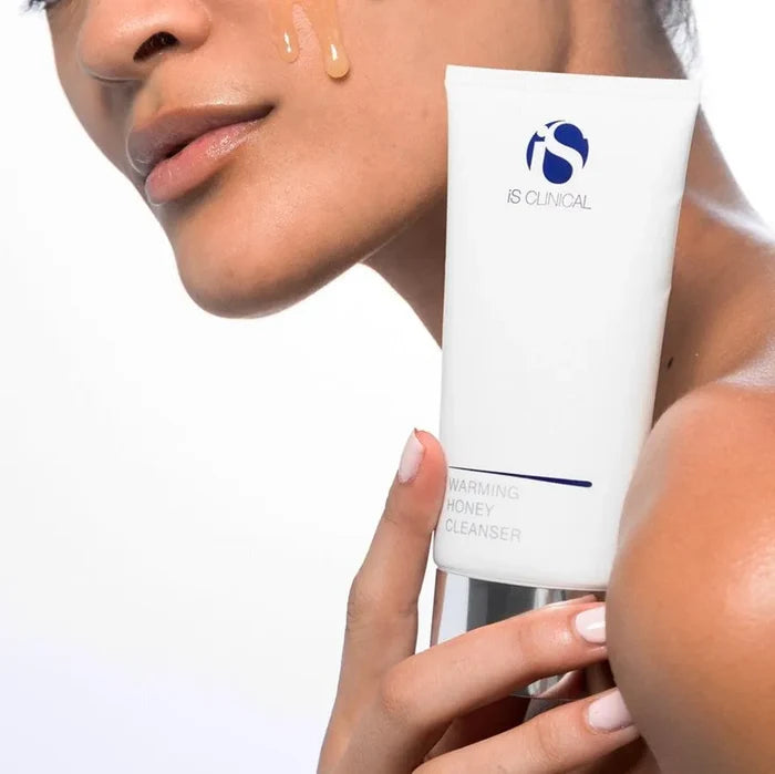 Close-up of a person holding iS Clinical Warming Honey Cleanser tube with honey-coloured cleanser on cheek