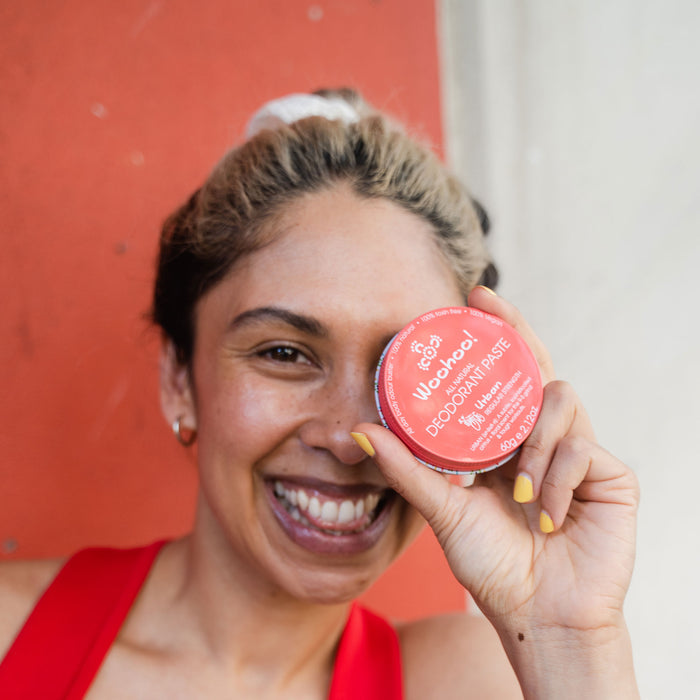 Woohoo Natural Deodorant Paste (Urban) 60g held by a smiling person against a red background.