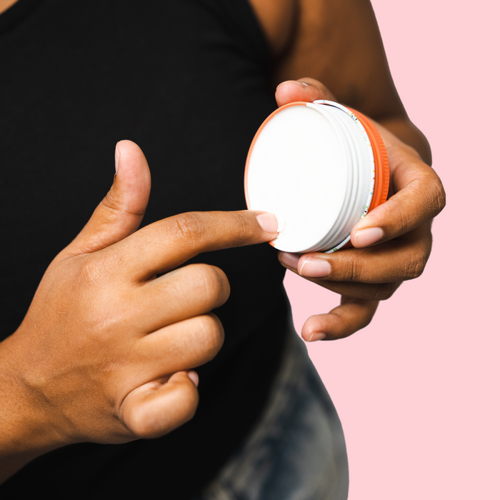 Woohoo Natural Deodorant Paste (Urban) in a hand, showcasing the orange lid and white paste inside.
