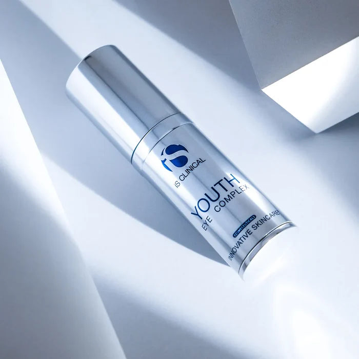Silver cylindrical bottle of iS Clinical Youth Eye Complex on white surface with angular shadows