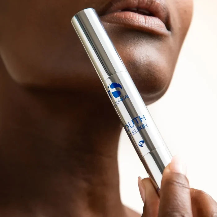 Hand holding iS Clinical Youth Lip Elixir silver tube near lips and chin on light background